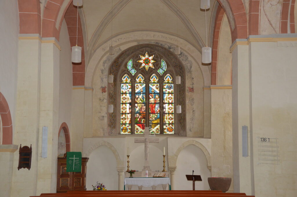 Altar in der Klosterkirche Flechtdorf. Mit Kerzen und Jesus am Kreuz. Rechts Taufstein, links die Kanzel. Im Hintergrund ein wunderschönes buntes Kirchenfenster.