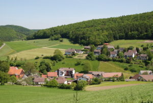 Ortsteil Benkhausen von einem Hügel aufgenommen. Man sieht einige Häuser umgeben von Wiesen und Wäldern.