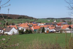 Ortsteil von Rhenegge. Vom Hang aus fotografiert. Häuser umrahmt von grünen Hügeln.