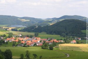 Ortsteil Stormbruch eingebettet in grüne Hügel, Täler und Wälder. Im Hintergrund der Diemelsee.