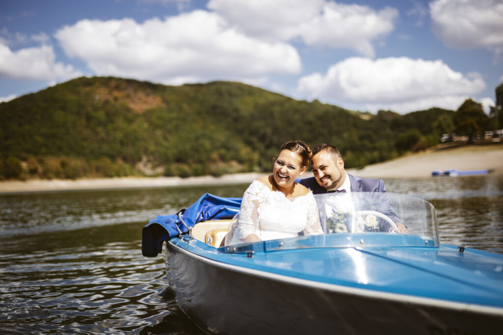 Hochzeitspaar lachend in einem blauen Elektroboot auf dem Diemelsee.