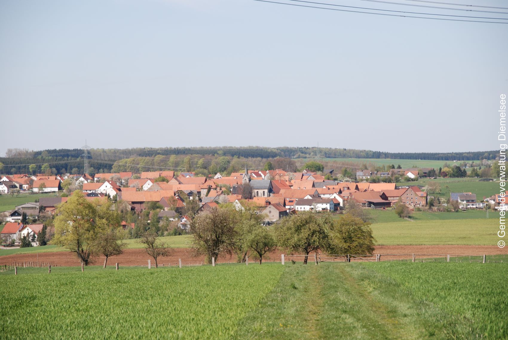 Ortsteil Vasbeck. Einige Häuser mit roten Dächern, in der Mitte die Vasbecker Kirche. Umgeben von Feldern und Wäldern.