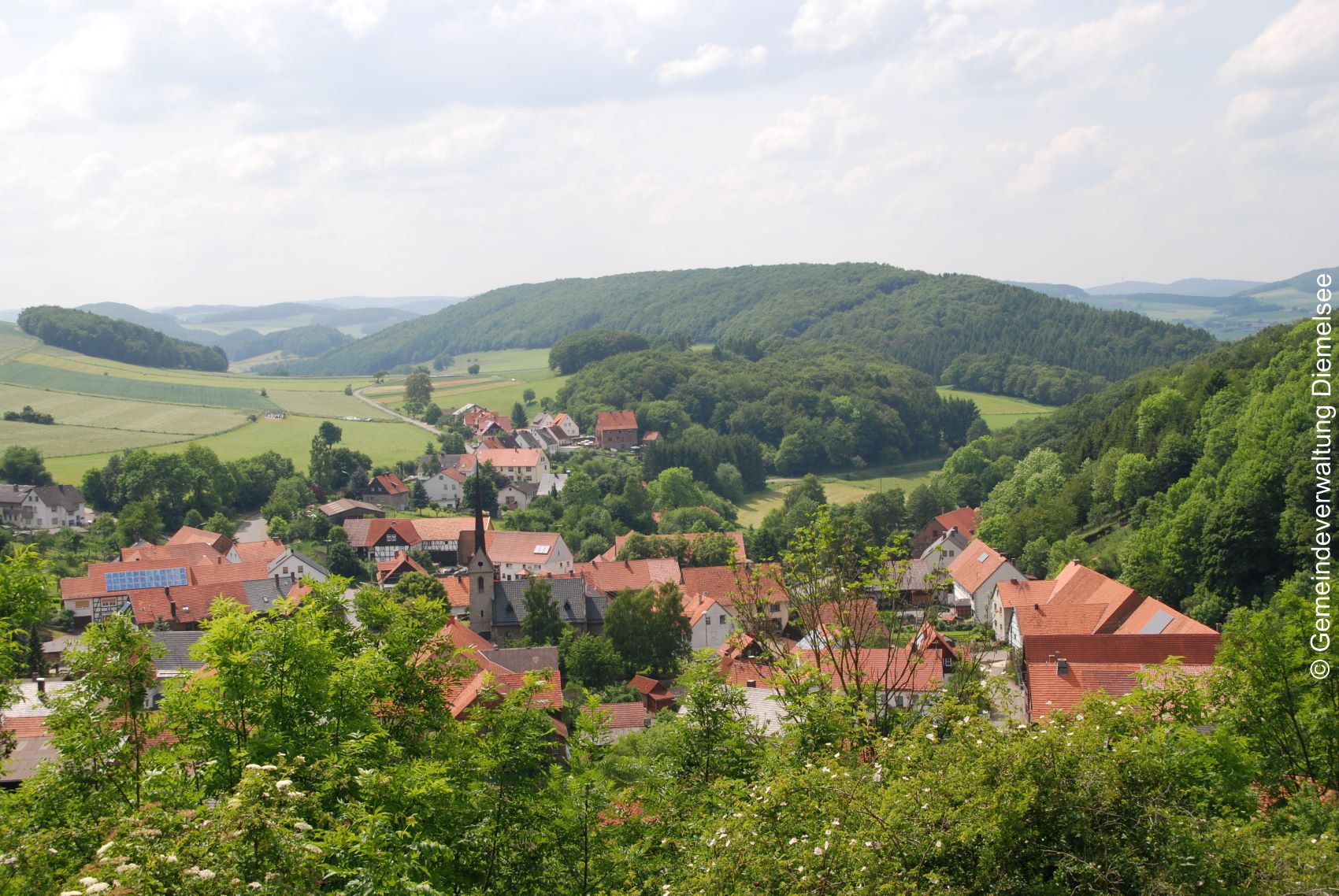 Ortsteil Wirmighausen, Häuser mit roten Dächern, in der Mitte die Kriche. Umgeben von Wiesen und grünen Wäldern.
