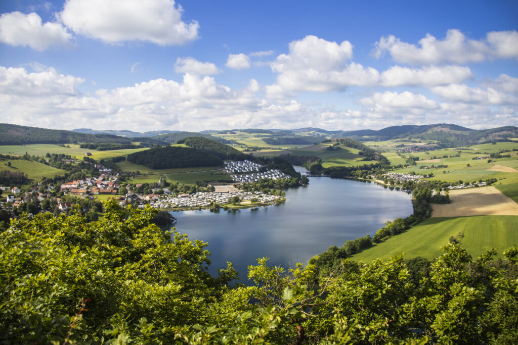 Ein Seitenarm vom Diemelsee mit der Stormbrucher Brücke und dem Ort Heringhausen mit dem Feriendorf fotografiert von der Klippe St. Muffert, Drum herum grüne Hügel und Wälder!