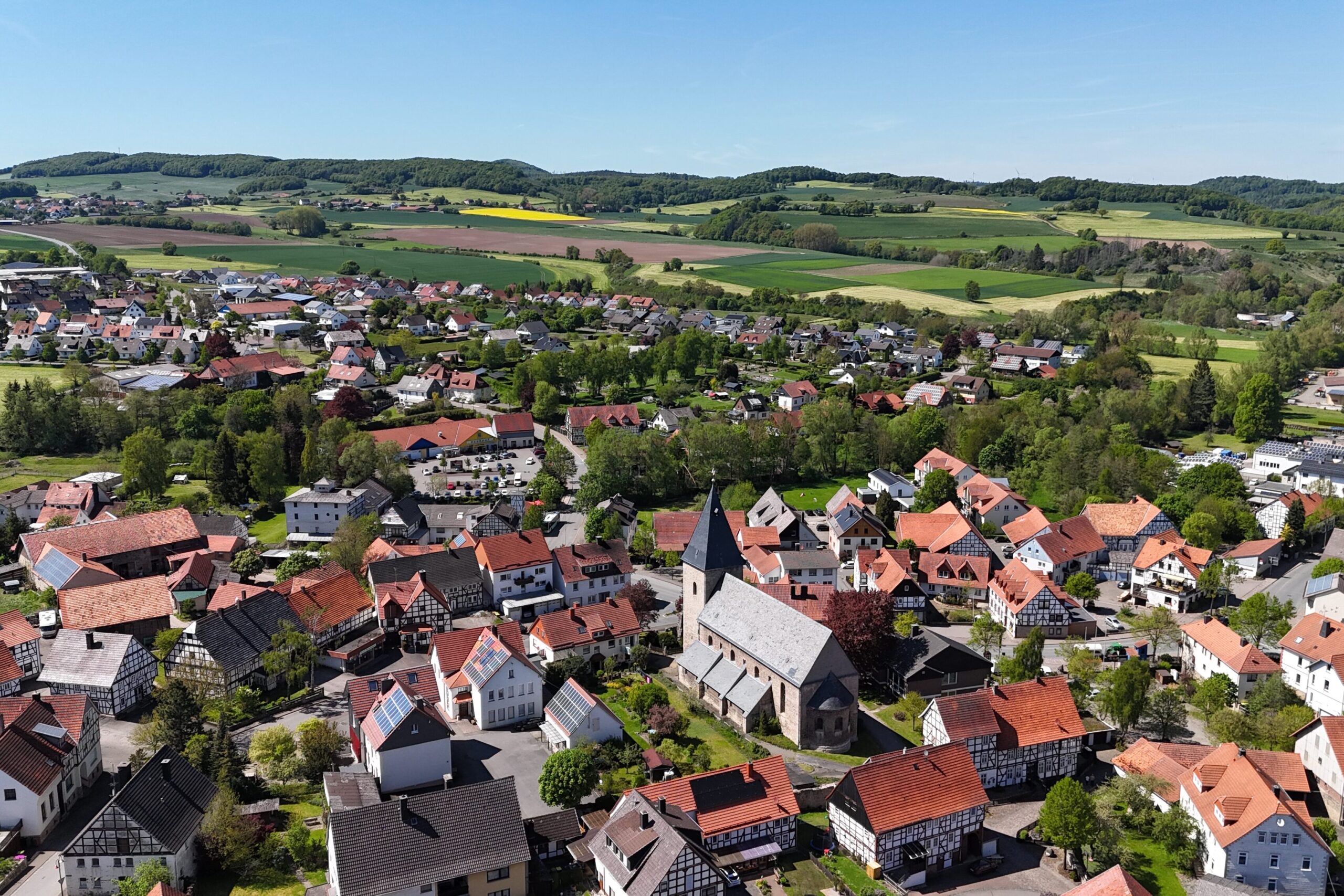 Ortsteil Adorf, Sitz der Gemeindeverwaltung. Ortskern mit der Kirche, rundherum viele Fachwerkhäuser, in der Ferne Neubaugebiet. Blick bis hin zum Nachbarort Rehnegge. Rundherum Wiesen und Wälder.